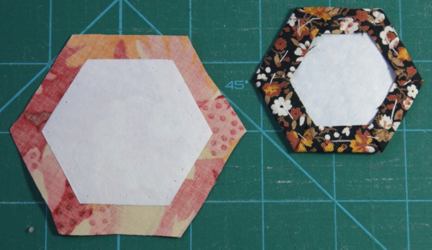 Hexagon on the left showing paper ironed in position and on the right a hexagon tacked and ready to sew.