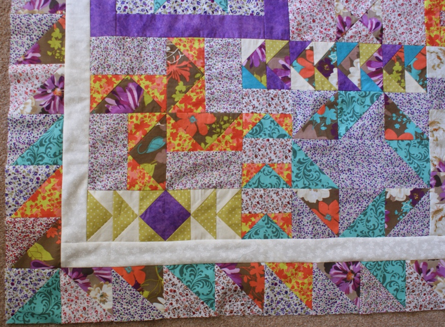 Two borders added: simple white on cream fabric to frame the puzzle blocks; and a border of half-square triangles made from the puzzle block fabrics.