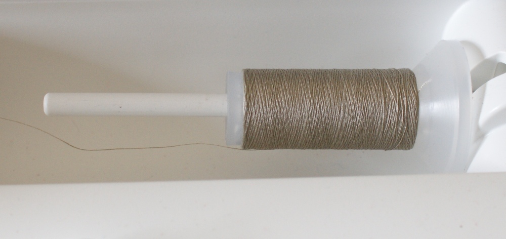 Thread wound onto a reel in a cross-weave fashion is designed to feed off the top of the reel.  It should be put on to the horizontal spool of a machine or threaded through a