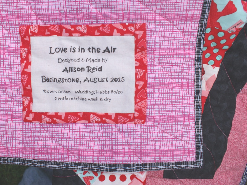 Label stitched to quilt and close up of the backing and binding fabrics ('Inprint' by Makower) bought at 'the Cotton Reel' Worcester.